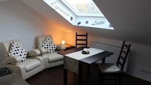 A cozy room with a sofa, a table, and a chair. There's a skylight with the words "Espresso" and "Latte" on it. - Pension Haselmann (Münster)