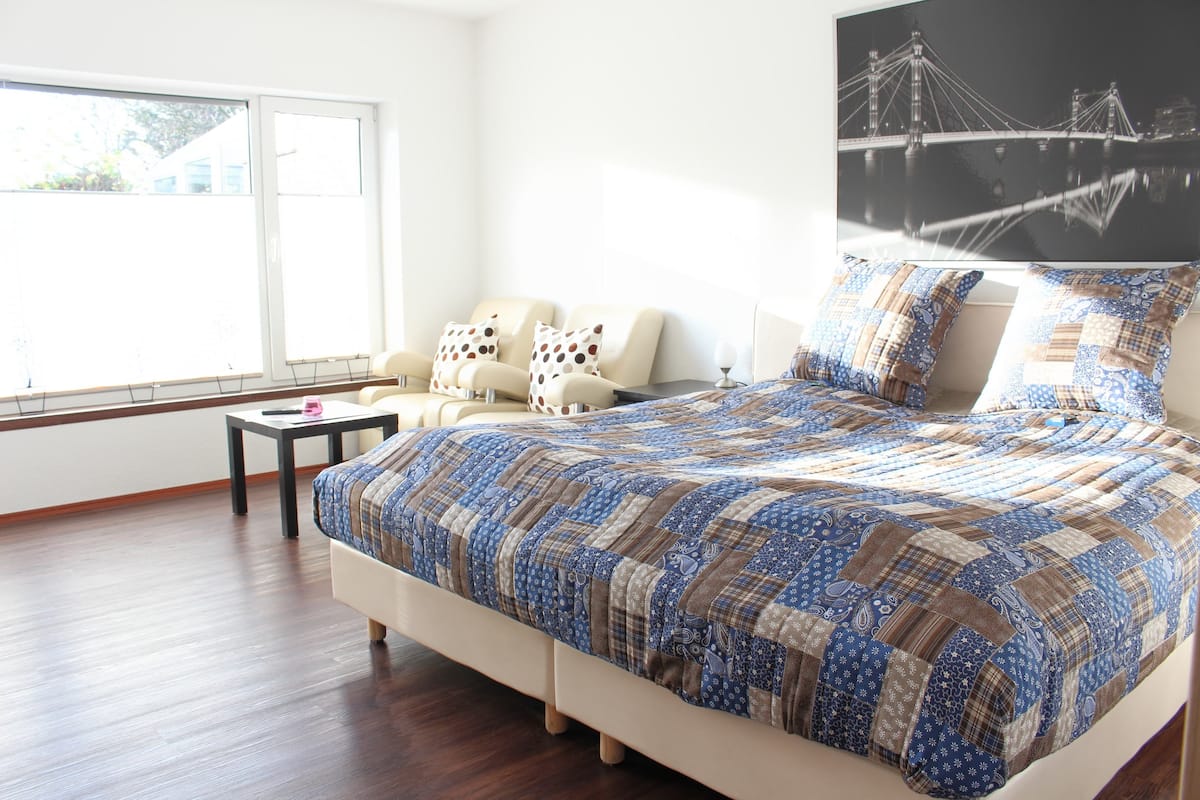Quarto com cama grande, sofá, mesa pequena e janela ampla.