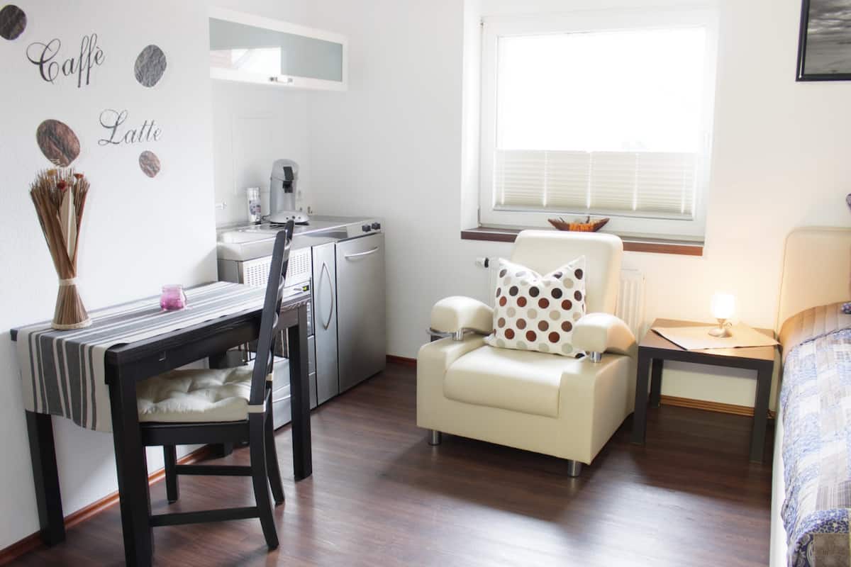 Quarto de hotel compacto com cozinha compacta, área de refeições com cadeira e mesa, sofá com almofada de bolinhas e cama com colcha estampada em azul.