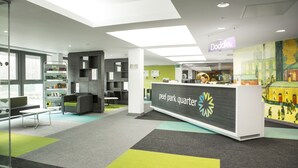 A modern reception area with a desk labeled "peel park quarter," a bookshelf, seating area, and a mural on the wall. - Peel Park Quarter - Campus Accommodation (Salford)