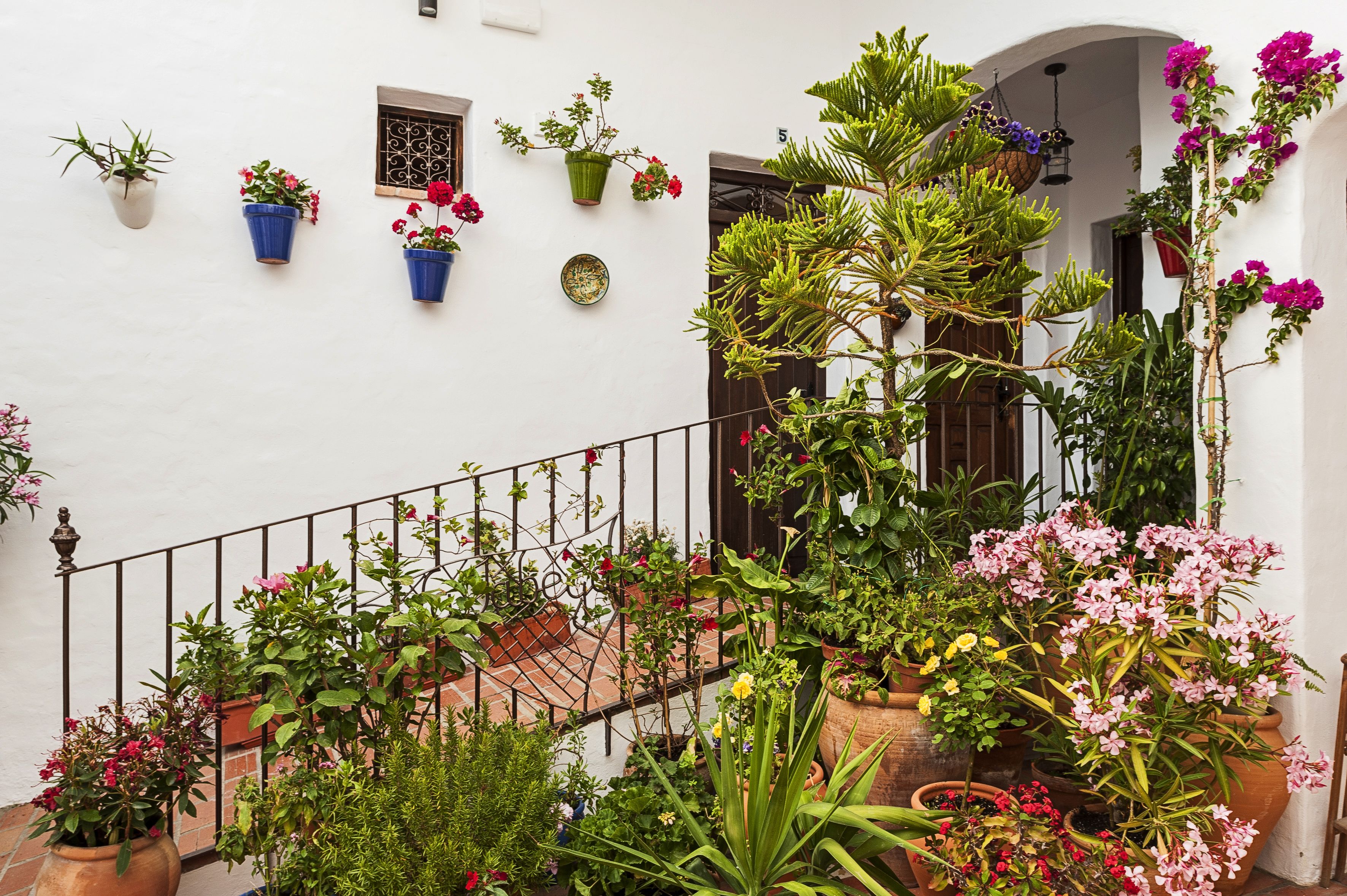 A white building with a tiled roof, a metal railing, and various potted plants and flowers.