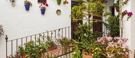 A white building with a tiled roof, a metal railing, and various potted plants and flowers.