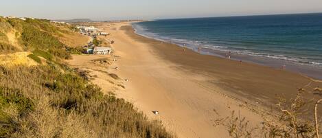 A coastal beach with a sandy shore, a few buildings, and a clear sky.