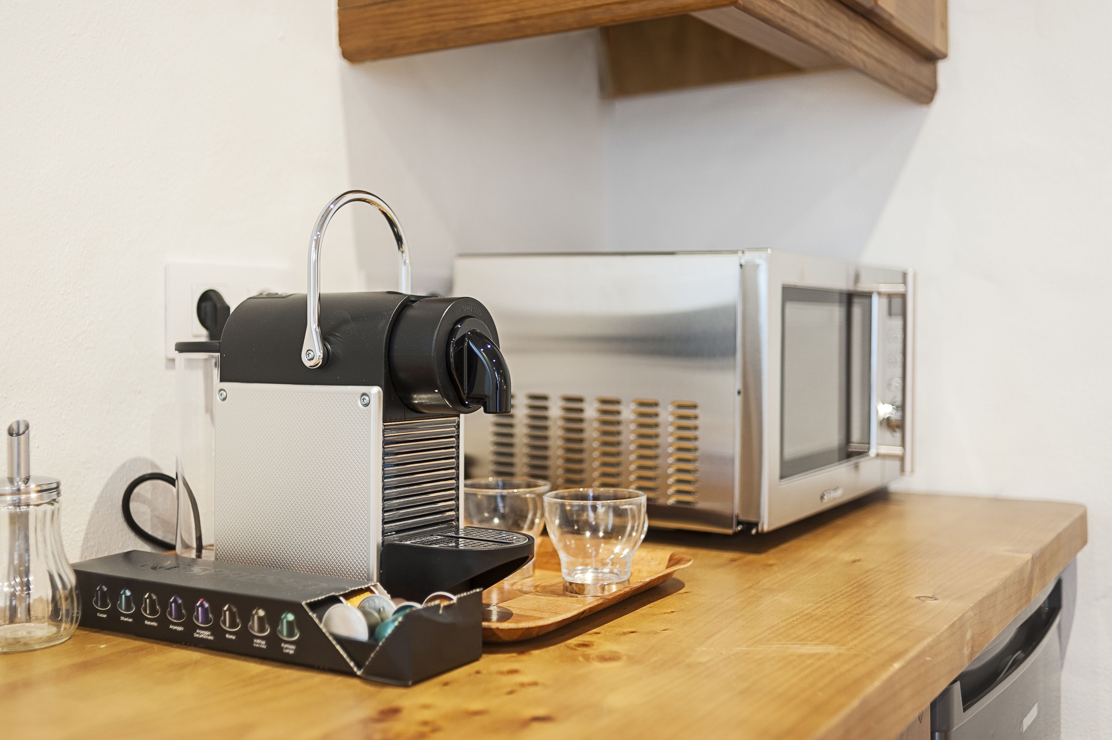 A kitchen with a coffee machine, a microwave, and two glasses on a wooden countertop.