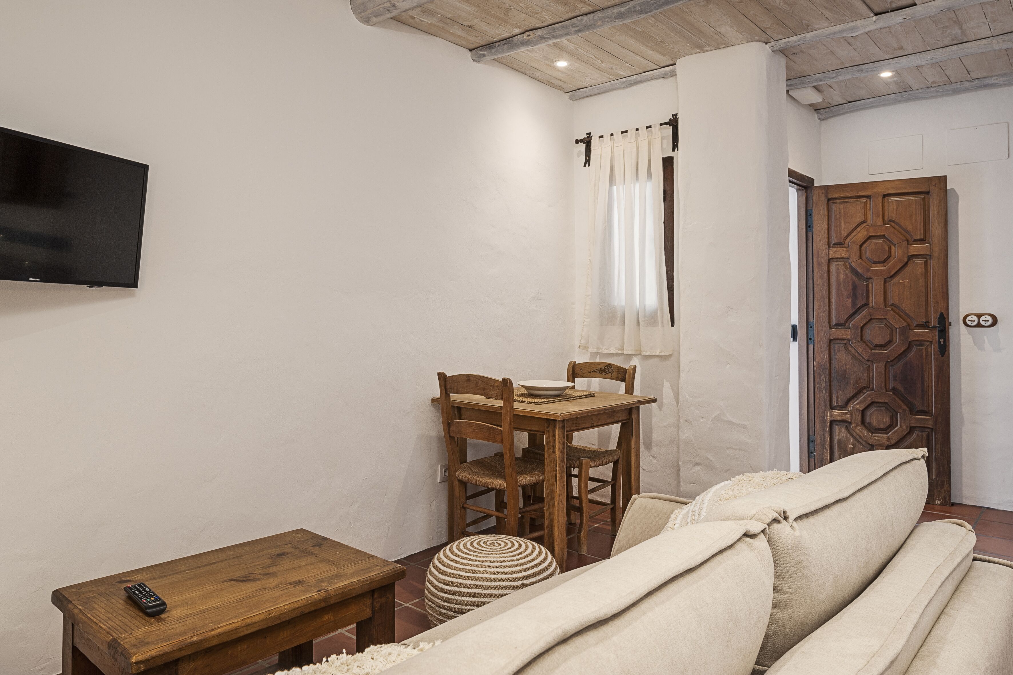A cozy room with a wooden table, chairs, a television, and a door with a geometric design.