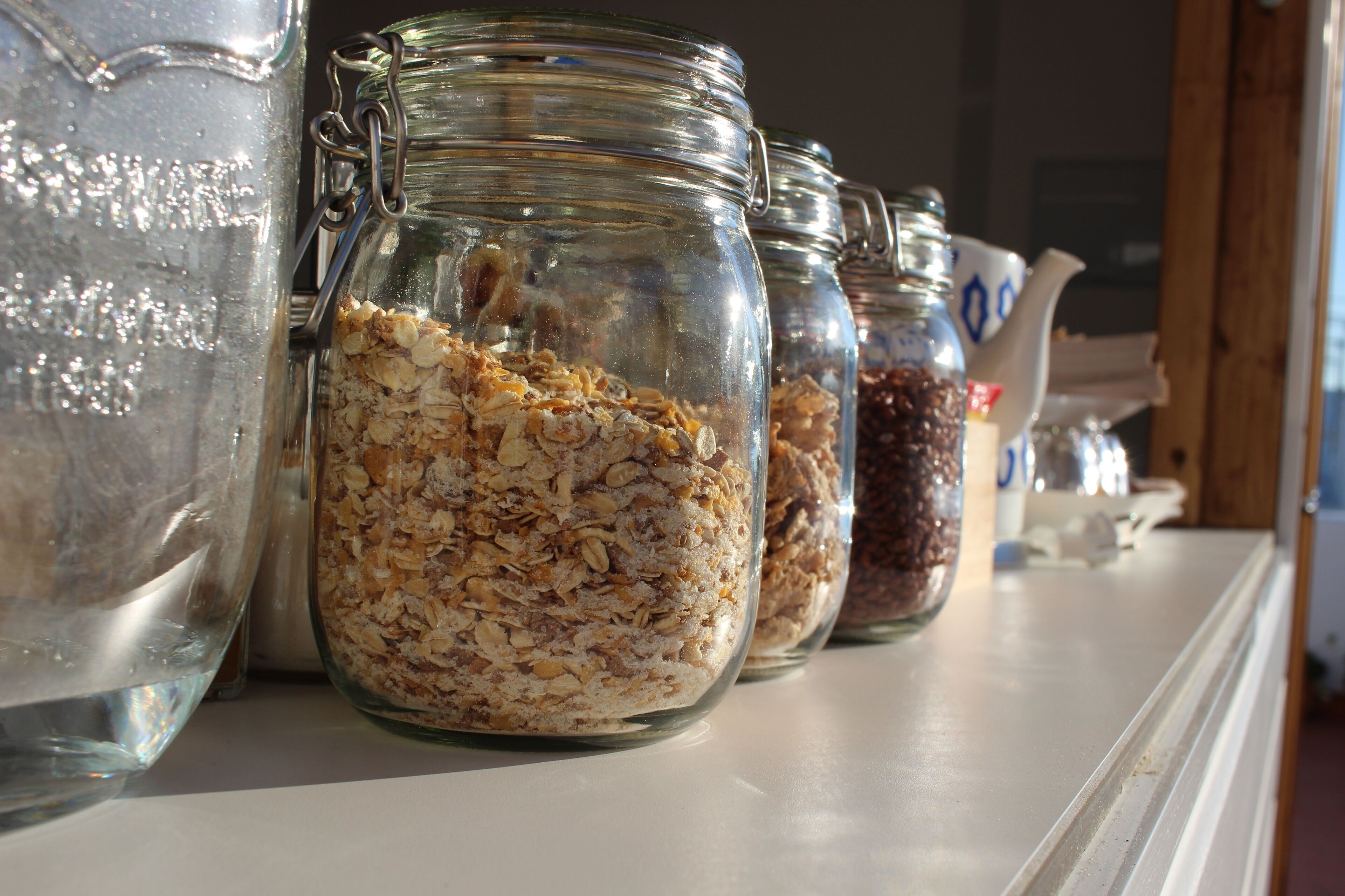 Una fila de frascos de vidrio llenos de diversos cereales y avena sobre una estantería.