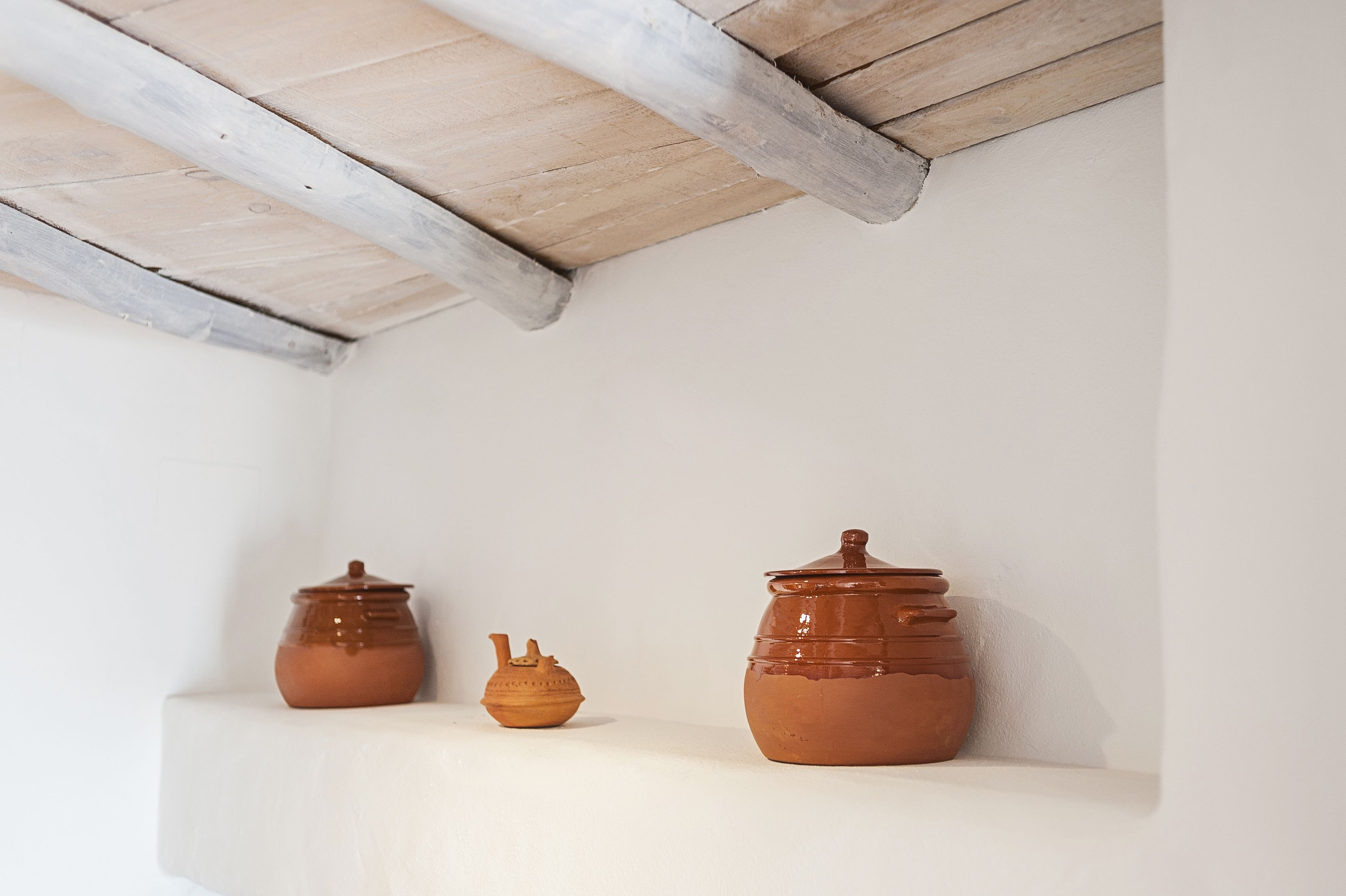 A corner with a white shelf holding two pottery items and a wooden ceiling beam.