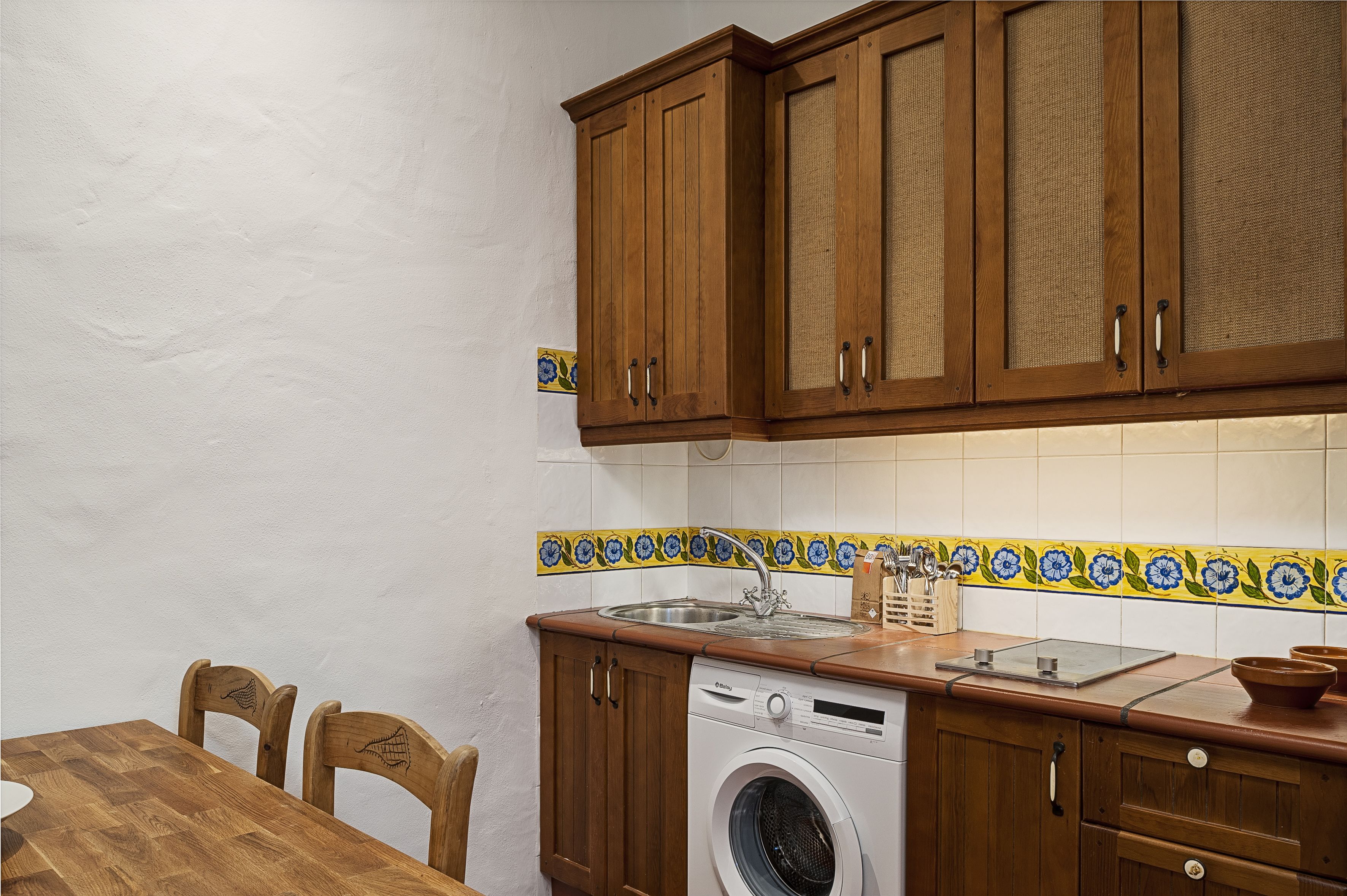 Een keuken met houten kastjes, een wasmachine en een betegelde spatwand.