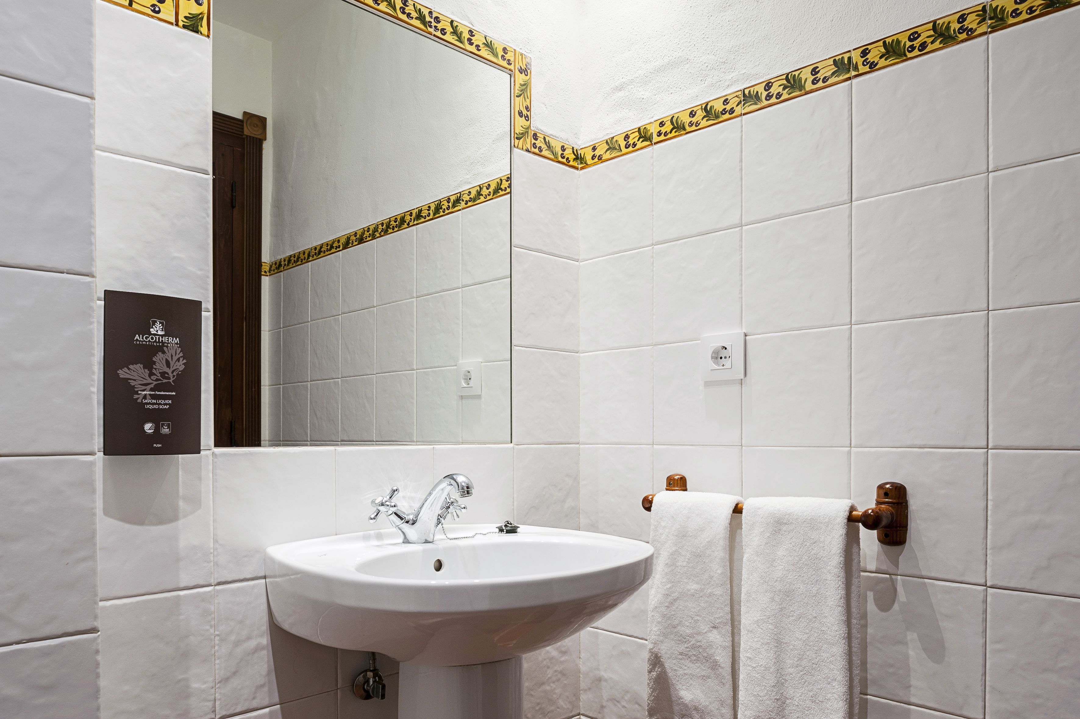 A bathroom with white tiles, a white sink, and a towel rack.