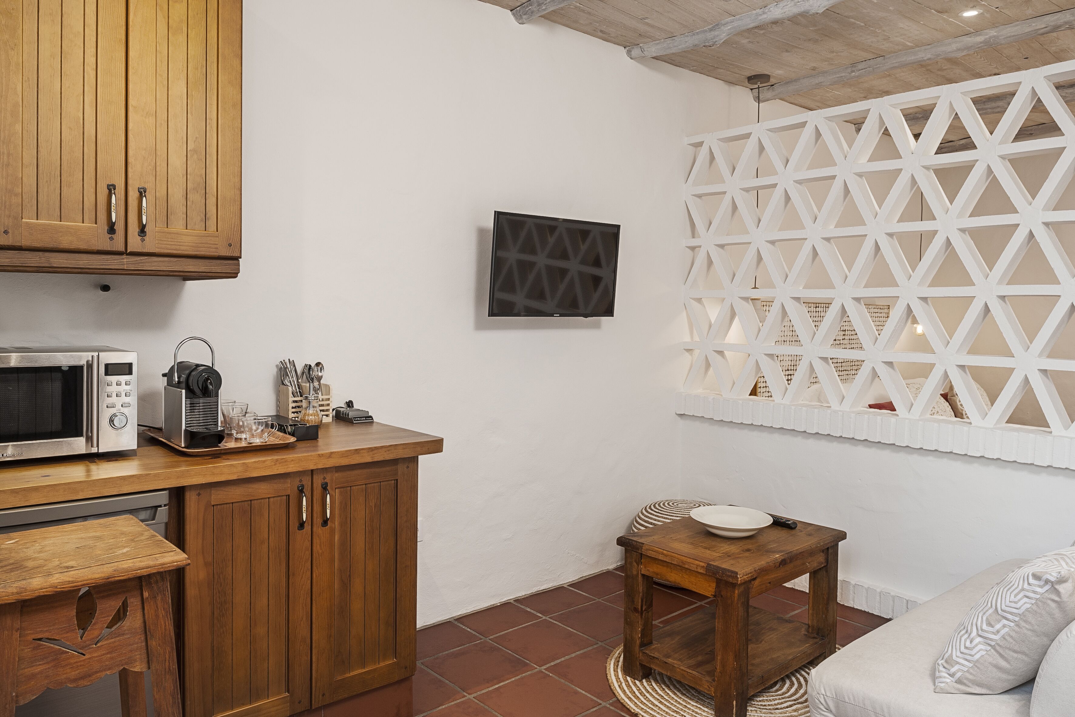 Una cocina con armarios de madera, un microondas y una cafetera. Hay una pequeña mesa de madera con un plato y un control remoto.