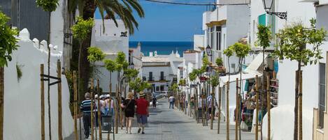 A narrow street lined with white buildings, palm trees, and a clear blue sky.
