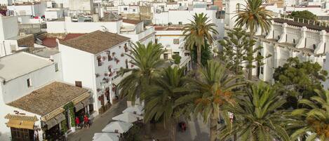 Un edificio blanco con cúpula y campanario, rodeado de palmeras y una calle con mesas al aire libre.