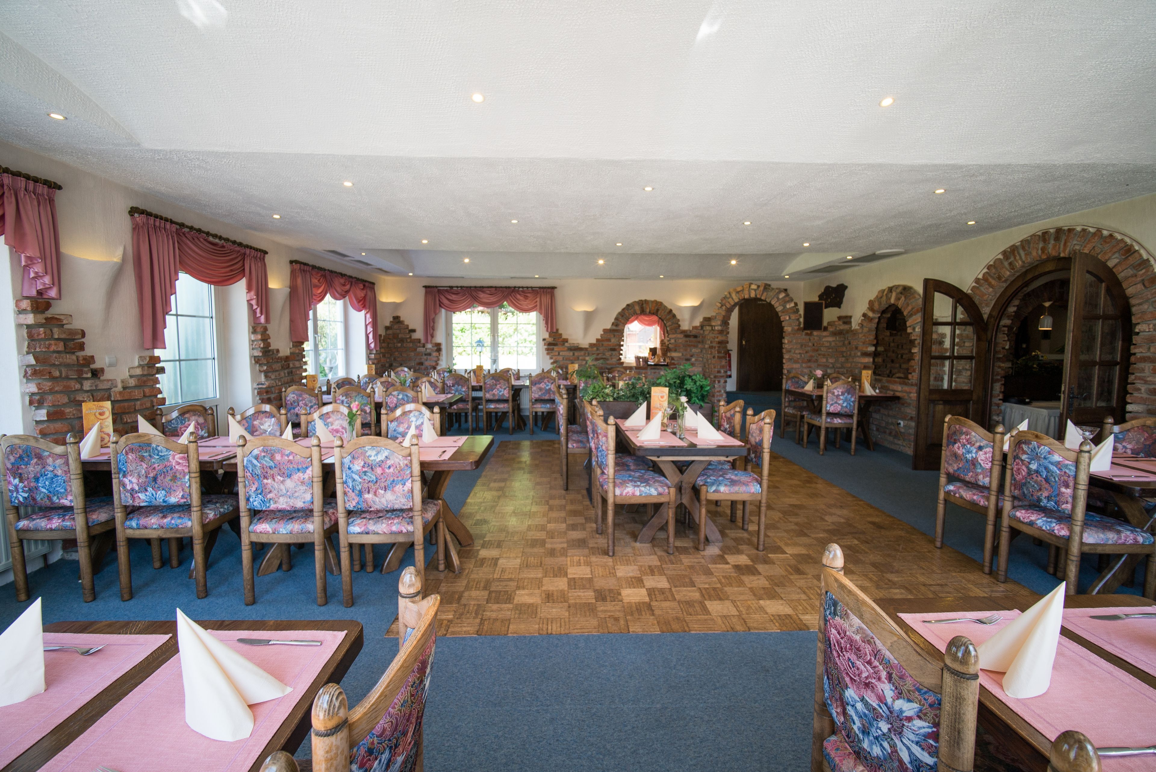 Restaurante com paredes de tijolo, mesas de madeira e cadeiras estampadas com flores.