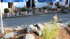 Un área de estar al aire libre con mesas y sillas de piedra, sombrillas azules y plantas en macetas.