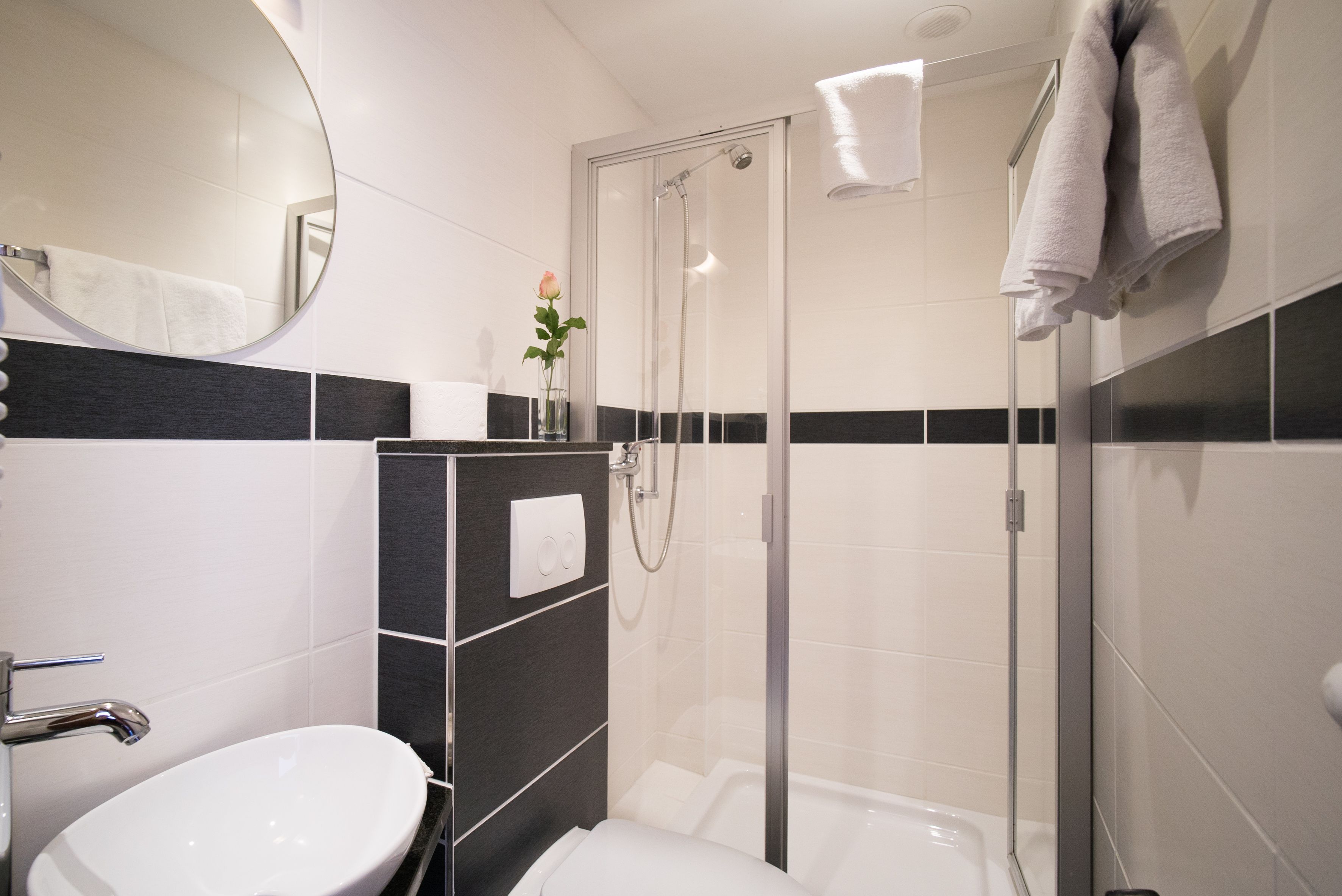 Un baño moderno con cabina de ducha acristalada, un lavabo blanco y un espejo.