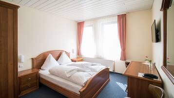 A hotel room with a wooden bed, a desk, a chair, and a wardrobe.