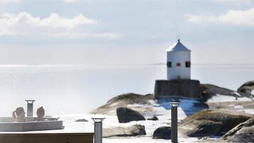 Une terrasse en bois offrant une vue sur une côte rocheuse et un phare situé au loin.