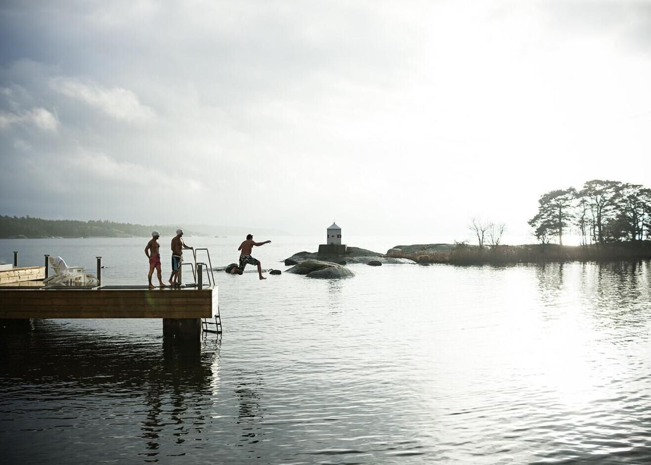 A pier extending into calm water with a lighthouse in the distance and trees on the far shore.