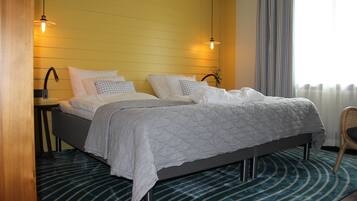 Un lit double avec une couette grise, une table de chevet avec une lampe et une fenêtre avec des rideaux.