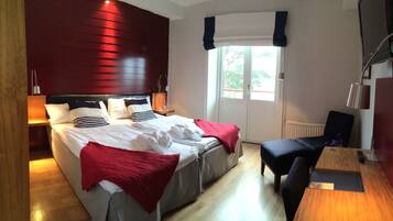 A hotel room with a large bed, bedside tables, a desk, and a window with curtains.