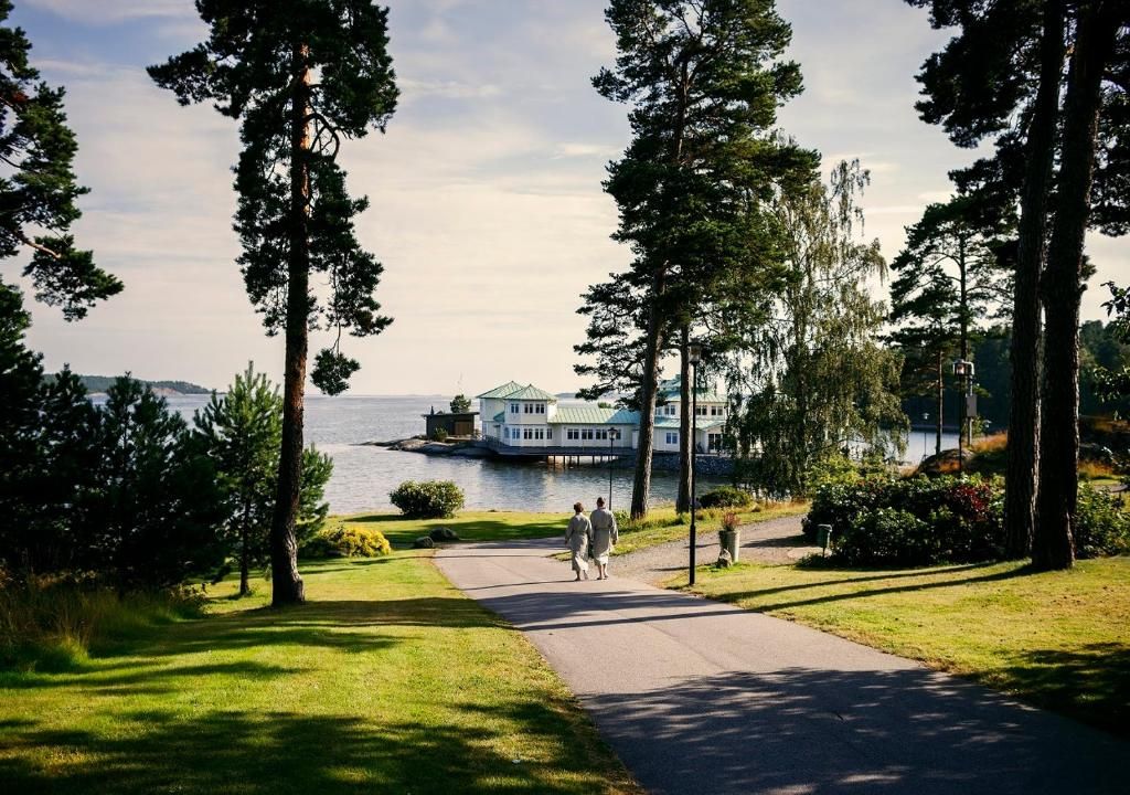 A pathway leading to a waterfront property with a large building, surrounded by trees and greenery.