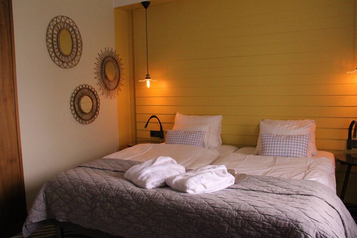 A neatly made bed with white linens and a gray quilt, a bedside lamp, and decorative wall mirrors.