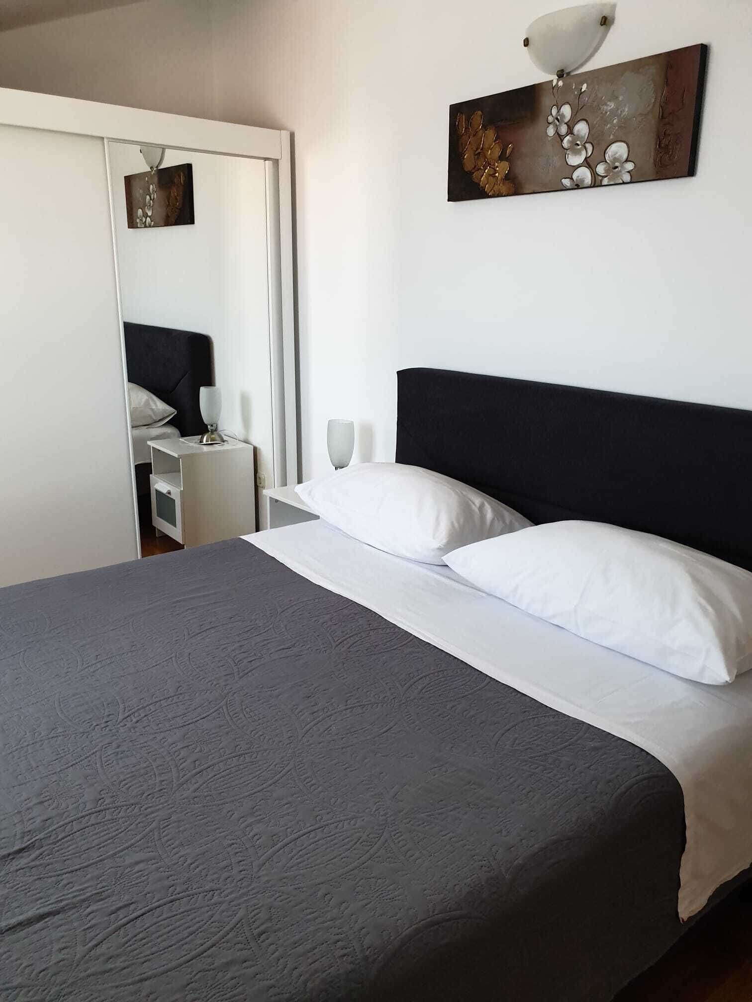 A neatly made bed with white pillows and a dark headboard, a bedside table with a lamp, and a wall-mounted artwork above the bed.