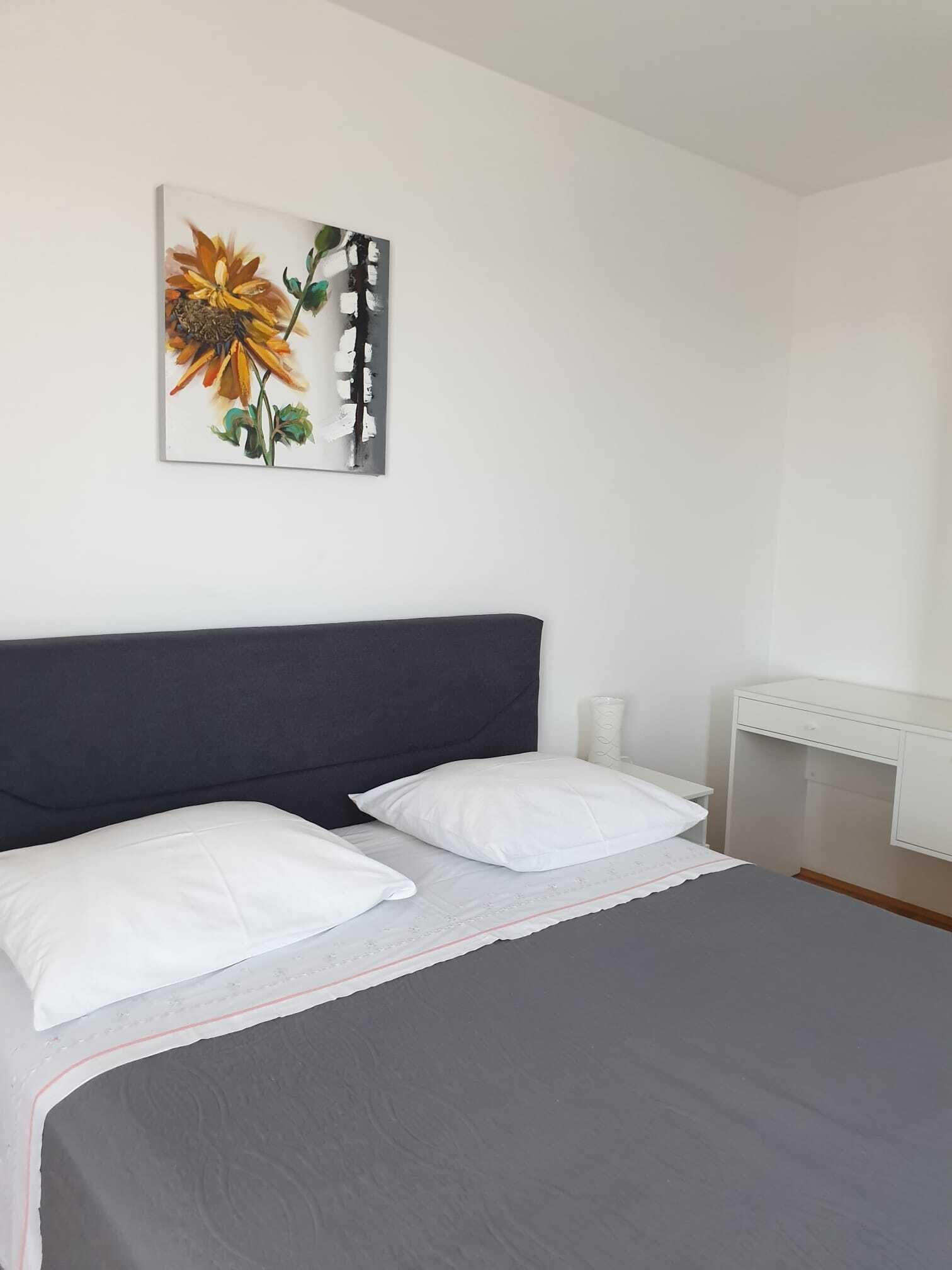 A bedroom with a bed, two pillows, a bedside table, a lamp, and a painting on the wall.