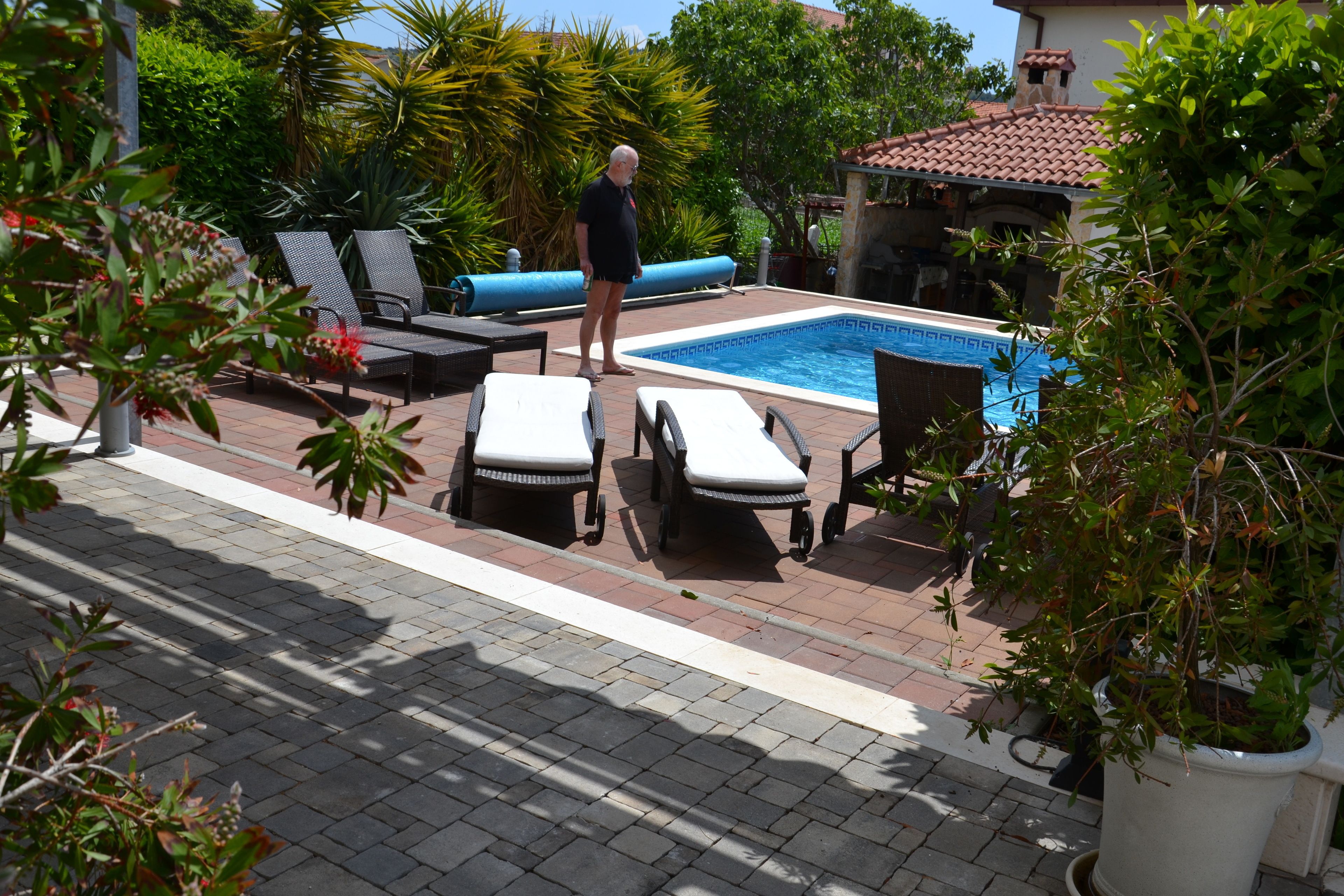 A pool area with lounge chairs and a man standing by the pool.