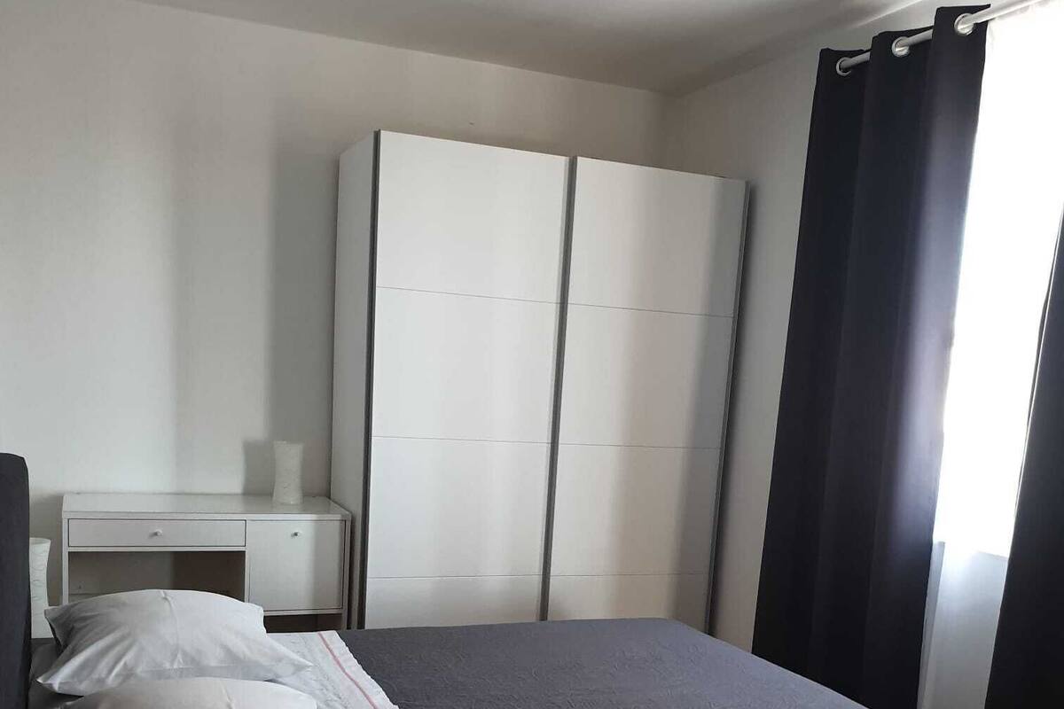 A bedroom with a bed, a nightstand, a wardrobe, and a window with curtains.