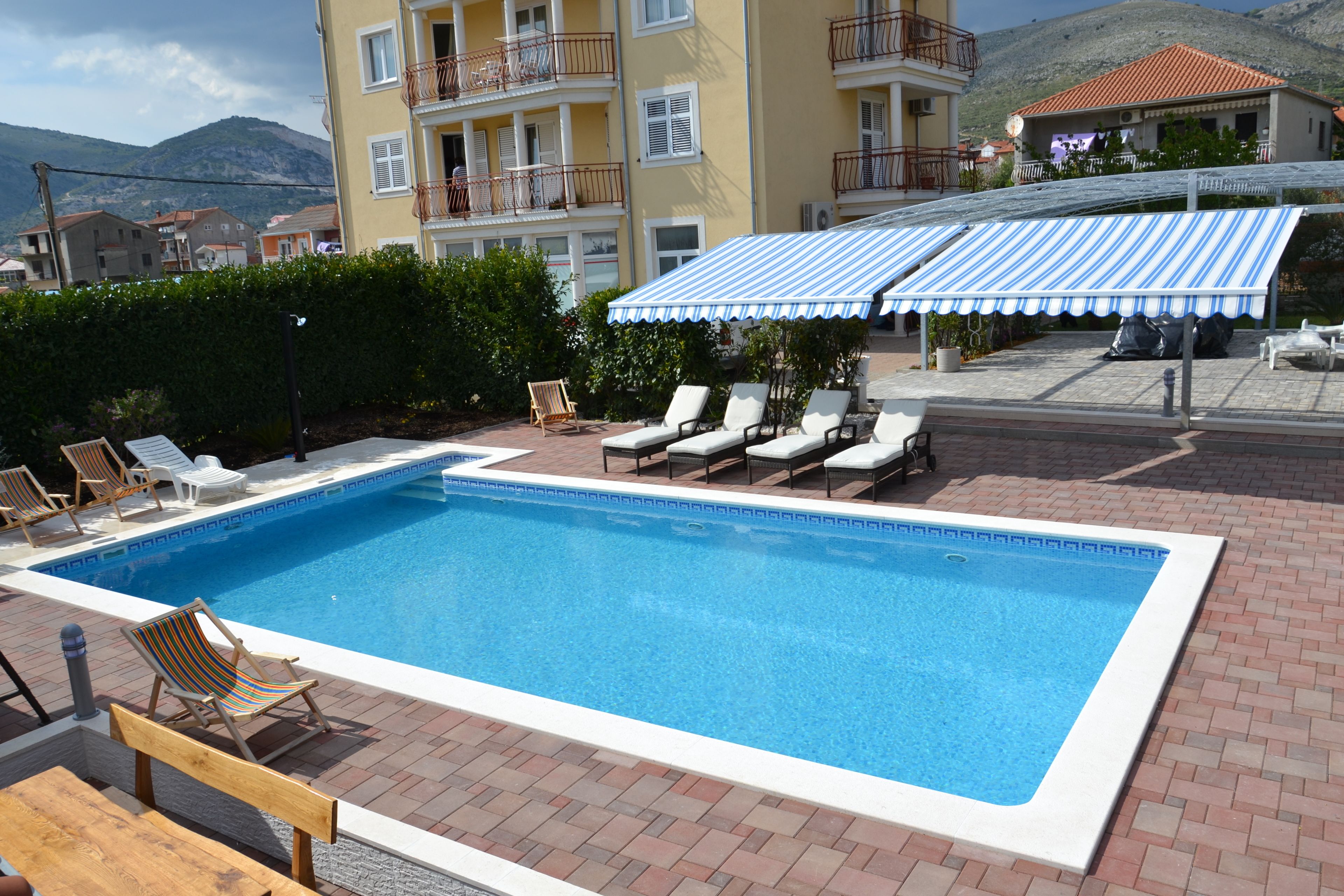 A rectangular swimming pool with lounge chairs and a striped awning.