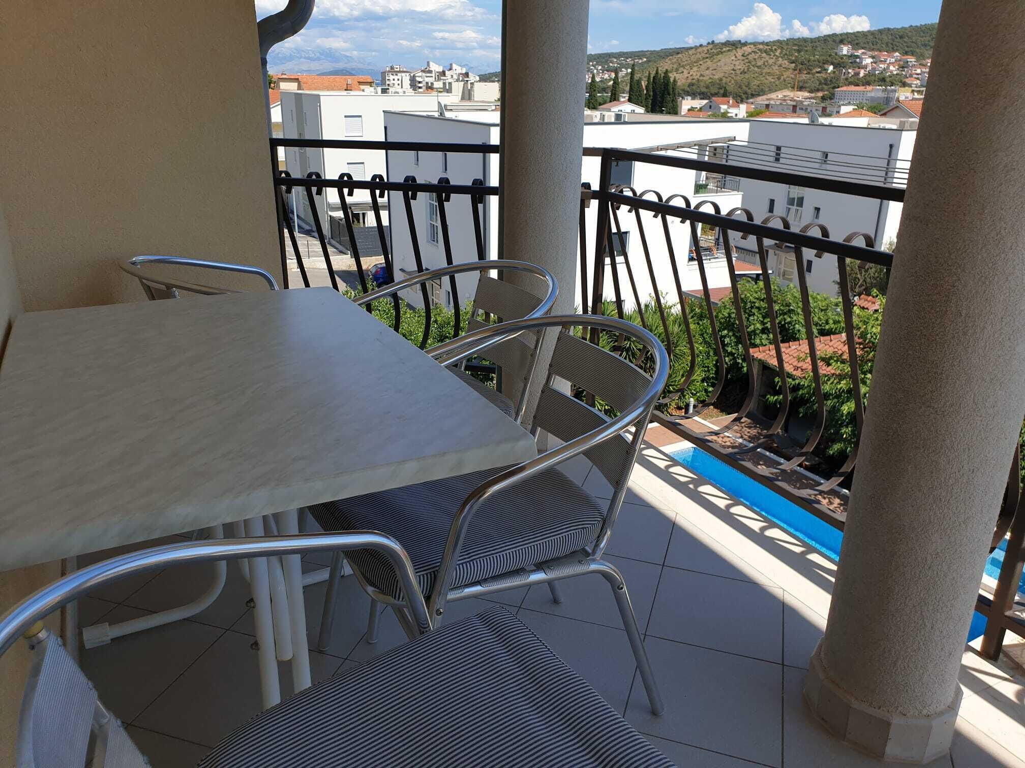 Un balcón con mesa y sillas, con vista a una piscina y edificios.