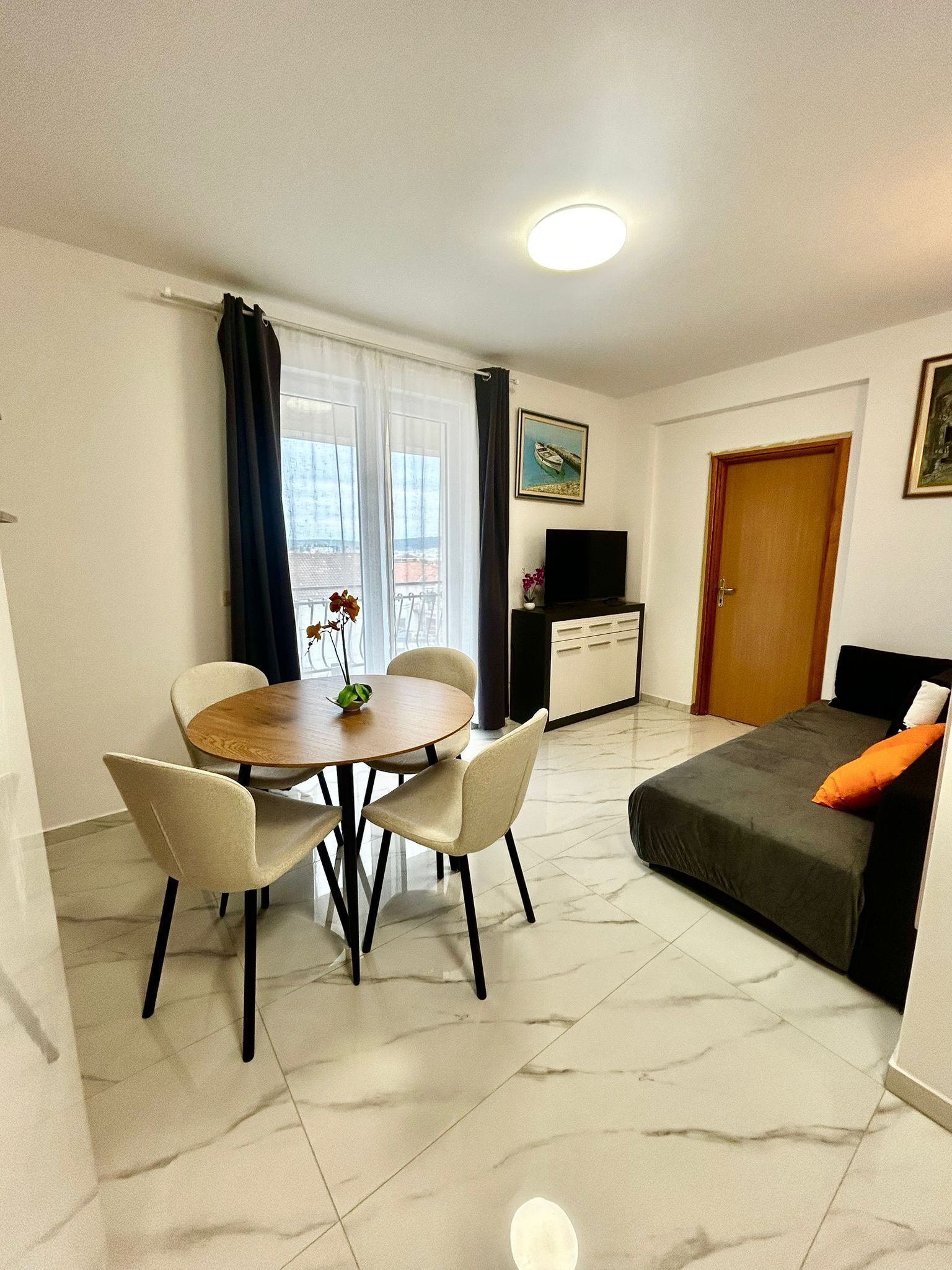 Ein modernes Wohnzimmer mit Esstisch, zwei Stühlen, einer Couch, einem Fernseher und einer Tür.