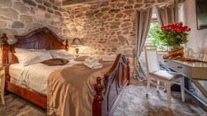 A bedroom with a stone wall, a wooden bed, a desk, and a chair. - Heritage Palace Varos - MAG Quaint & Elegant Boutique Hotels (Split)
