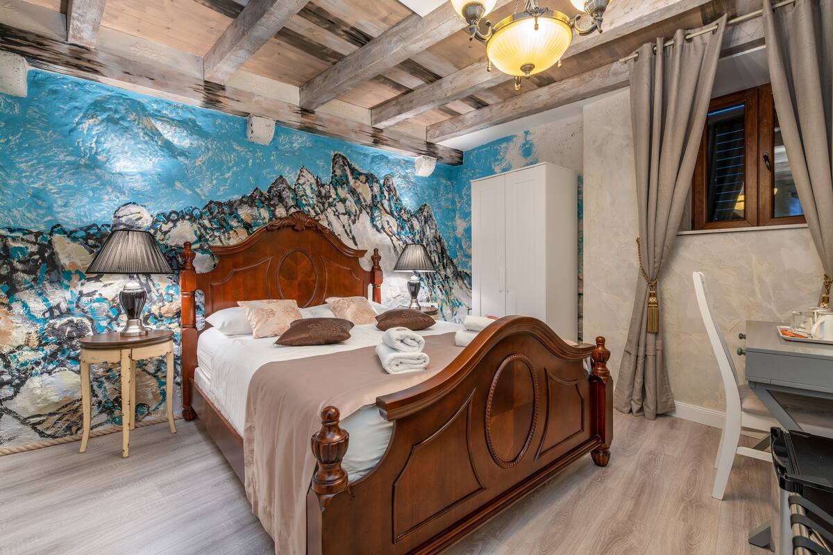 Ein Schlafzimmer mit einem hölzernen Bett, einem Nachttisch, einer Lampe und einer Wandmalerei.