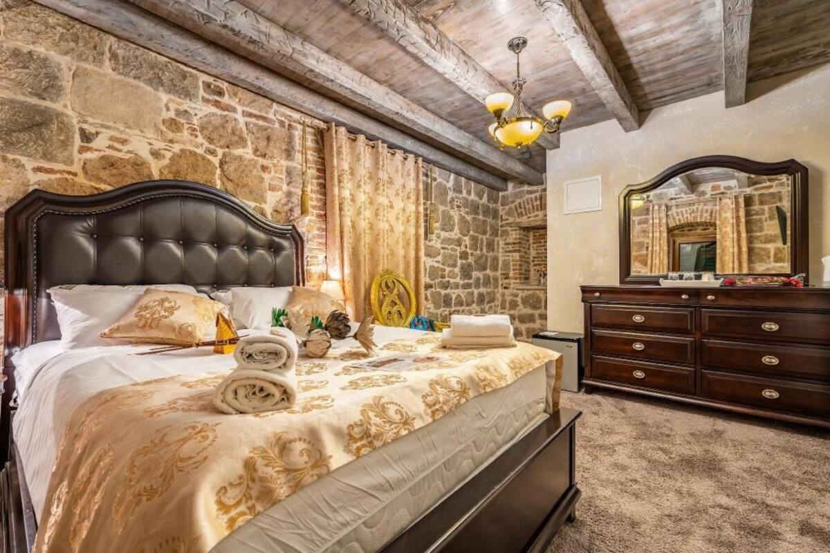 A bedroom with a stone wall, a wooden ceiling, a bed with a headboard, a dresser, and a mirror.