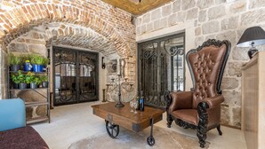 A room with a stone wall, a wooden table with a wine bottle, a chair, and a lamp. - Heritage Palace Varos - MAG Quaint & Elegant Boutique Hotels (Split)