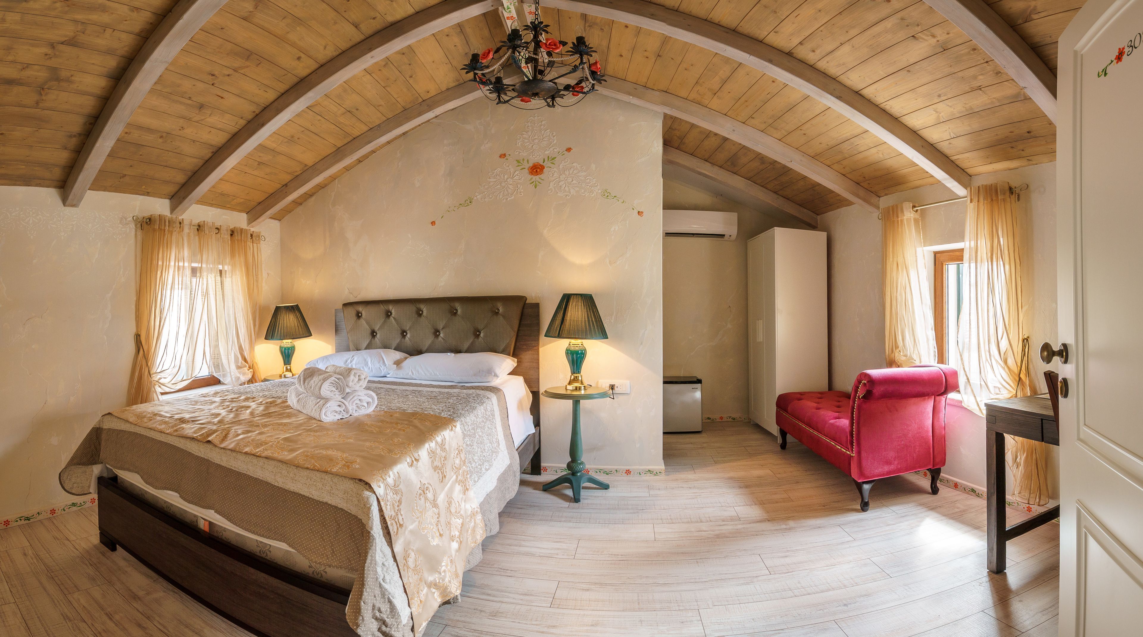 A bedroom with a large bed, two bedside lamps, a red chair, and a chandelier.