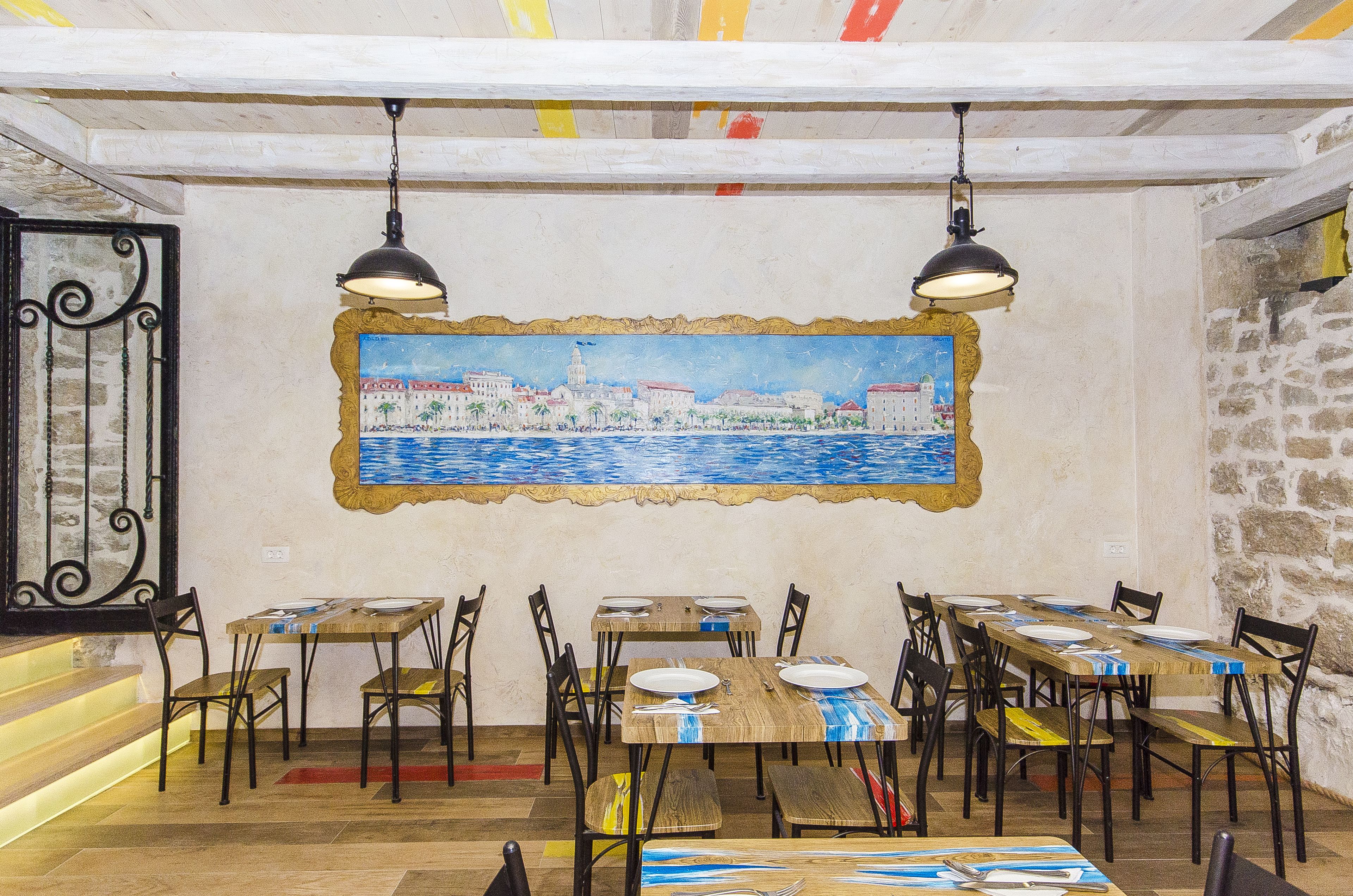 A dining area with tables set for four, wooden chairs, and a mural of a coastal cityscape on the wall.