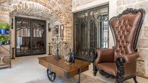 A room with a stone wall, a wrought iron gate, a wooden coffee table with wine glasses, and a leather armchair. - Heritage Palace Varos - MAG Quaint & Elegant Boutique Hotels (Split)