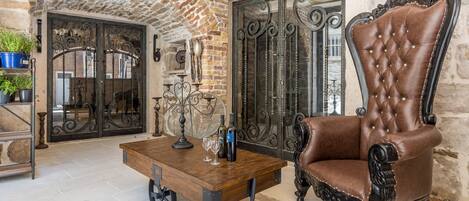 A room with a stone wall, a wrought iron gate, a wooden coffee table with wine glasses, and a leather armchair.