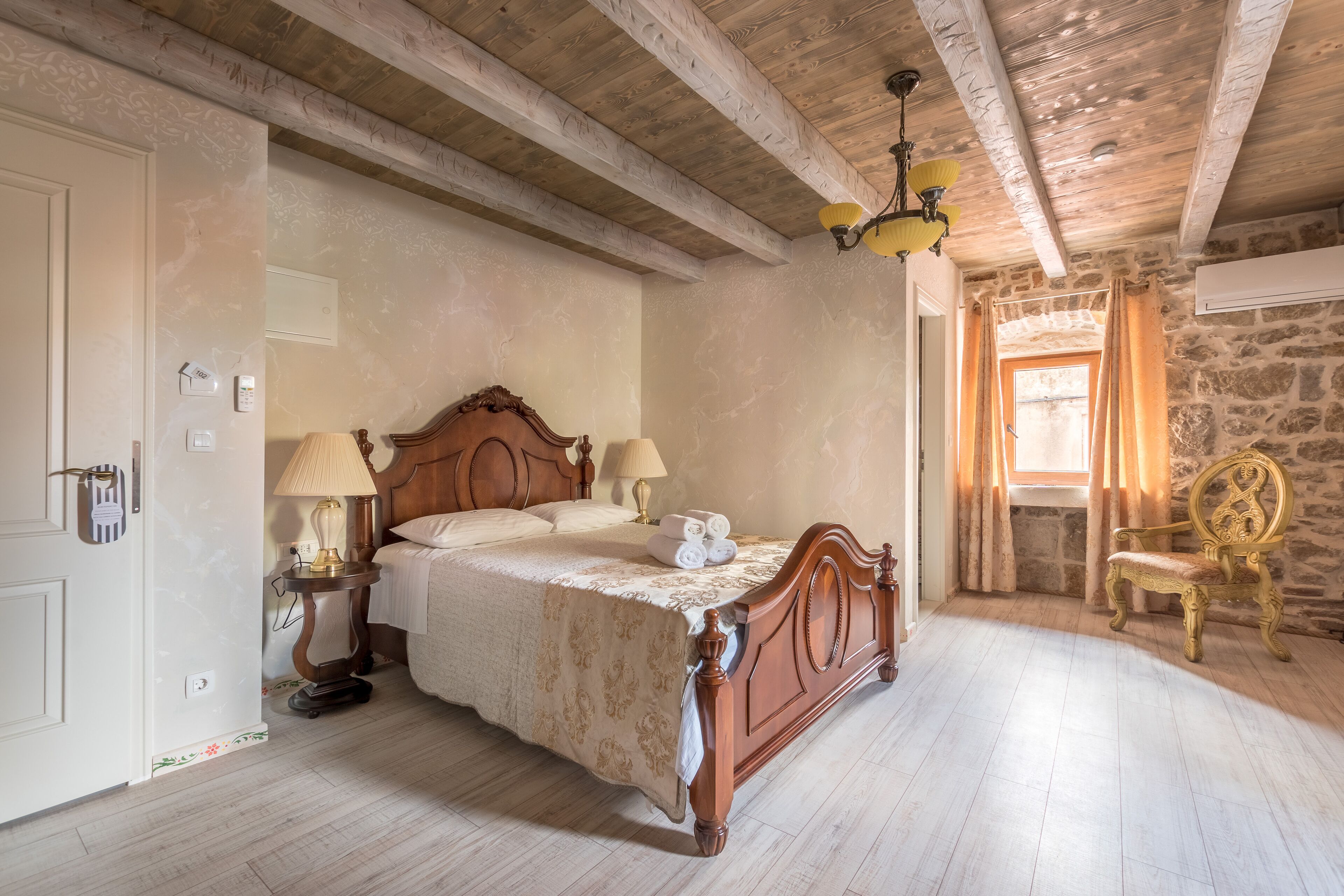 Een slaapkamer met een houten bed, een nachtkastje, een lamp, een stoel en een stenen muur.