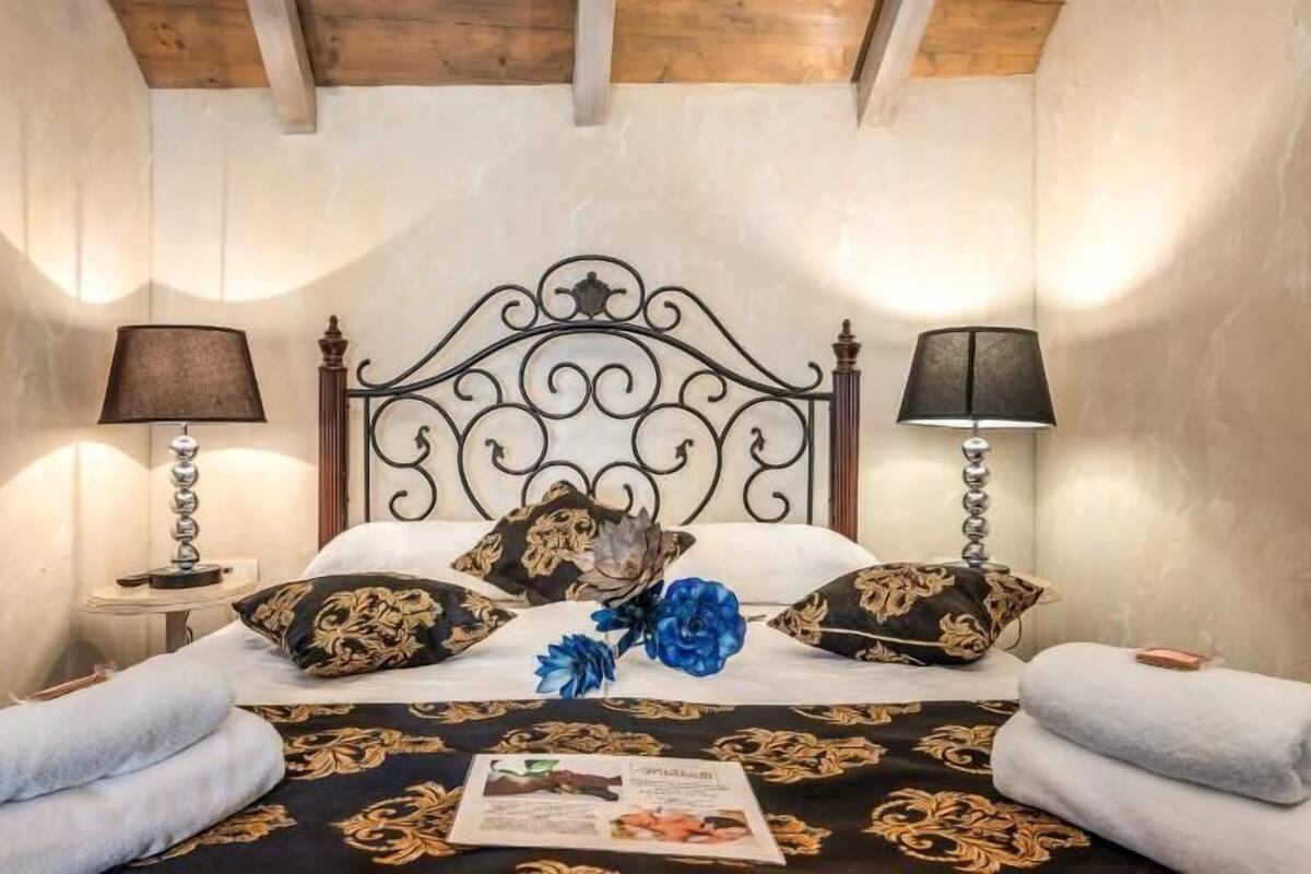 Ein Bett mit aufwendigem Kopfteil, zwei Nachttischlampen, Zierkissen und zusammengerollte Handtücher.