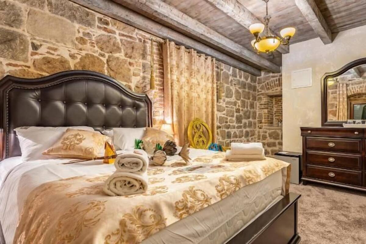 Ein Schlafzimmer mit Steinwand, einem Bett mit gestepptem Kopfteil, einem Schminktisch und einem Spiegel.