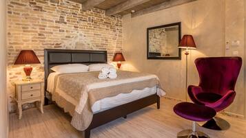 Un dormitorio con pared de ladrillo, una cama con cabecera, dos lámparas de noche, una silla roja y un espejo en la pared.