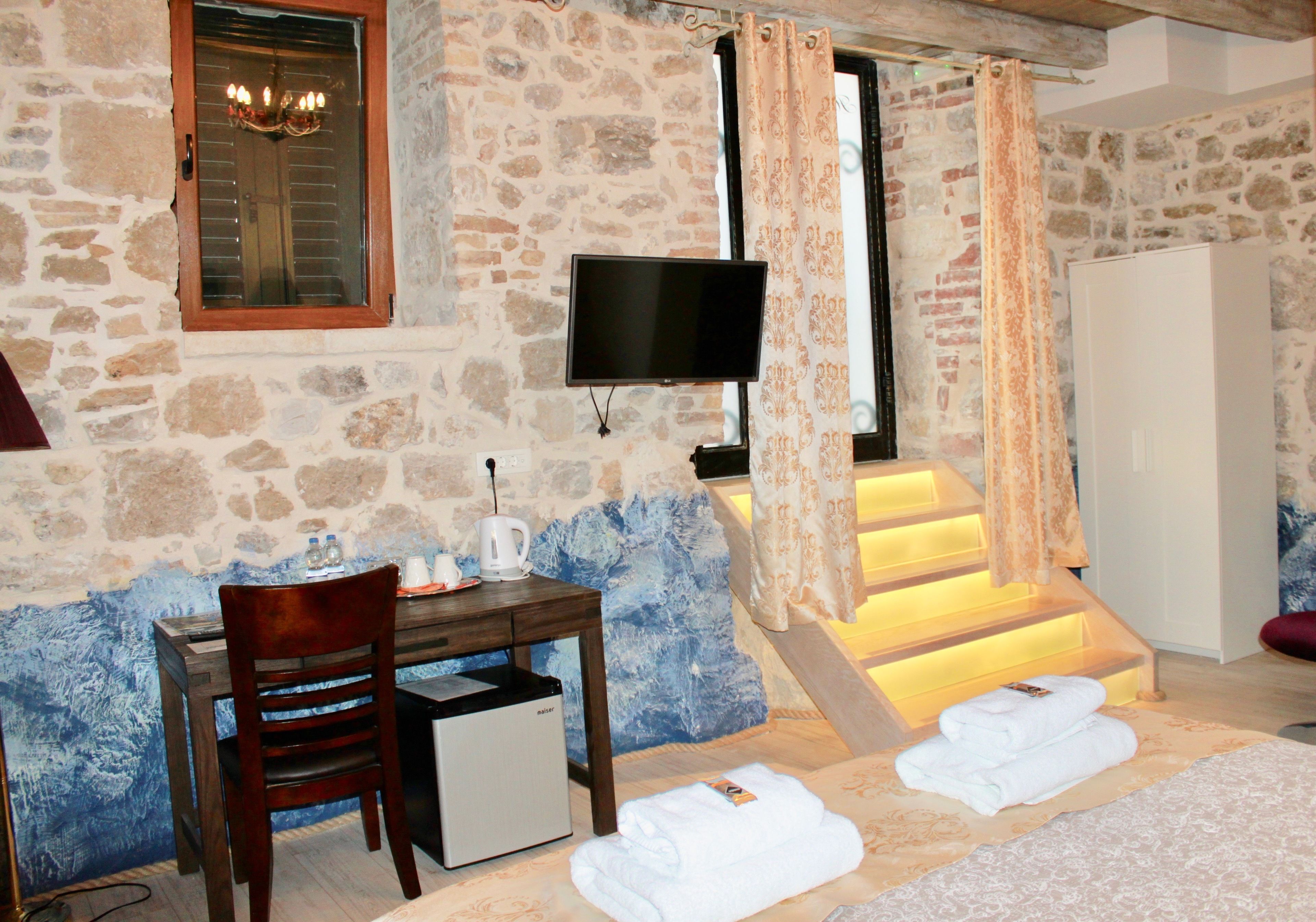 A stone-walled room with a wooden desk, a television, and a staircase with illuminated steps.