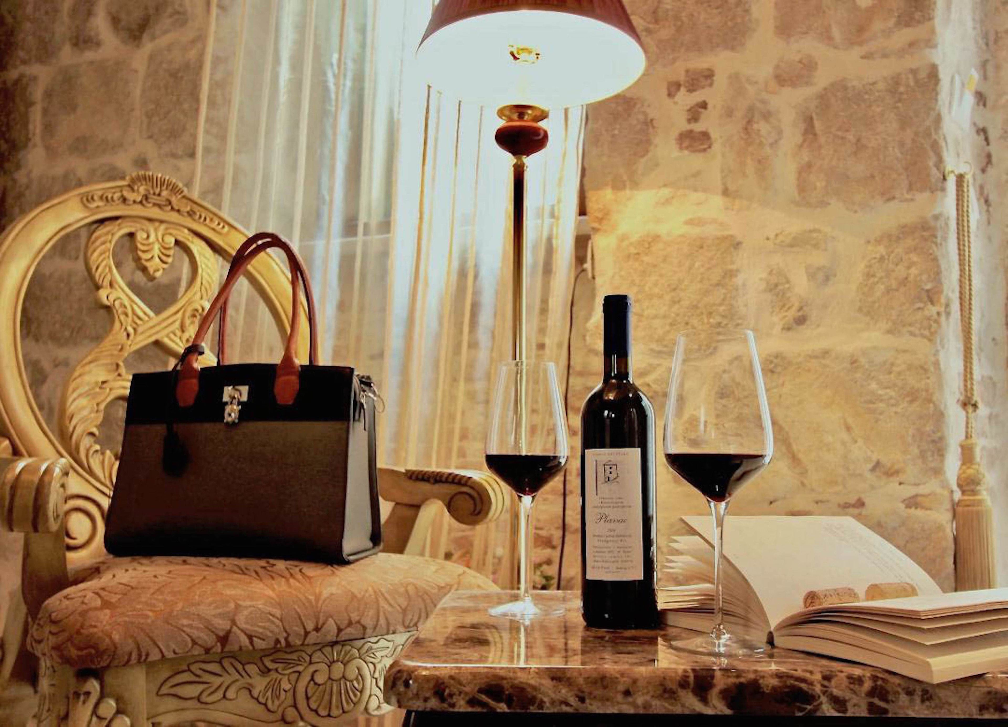A luxurious setting with a marble table, a bottle of wine, two wine glasses, a handbag, and an open book.