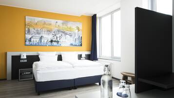 Habitación de hotel con una cama, un cuadro en la pared, un televisor, una mesita de noche con una botella y una ventana.
