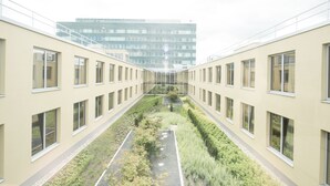 Een gang met een centrale tuin, moderne gebouwen aan weerszijden en een hoogbouw op de achtergrond.