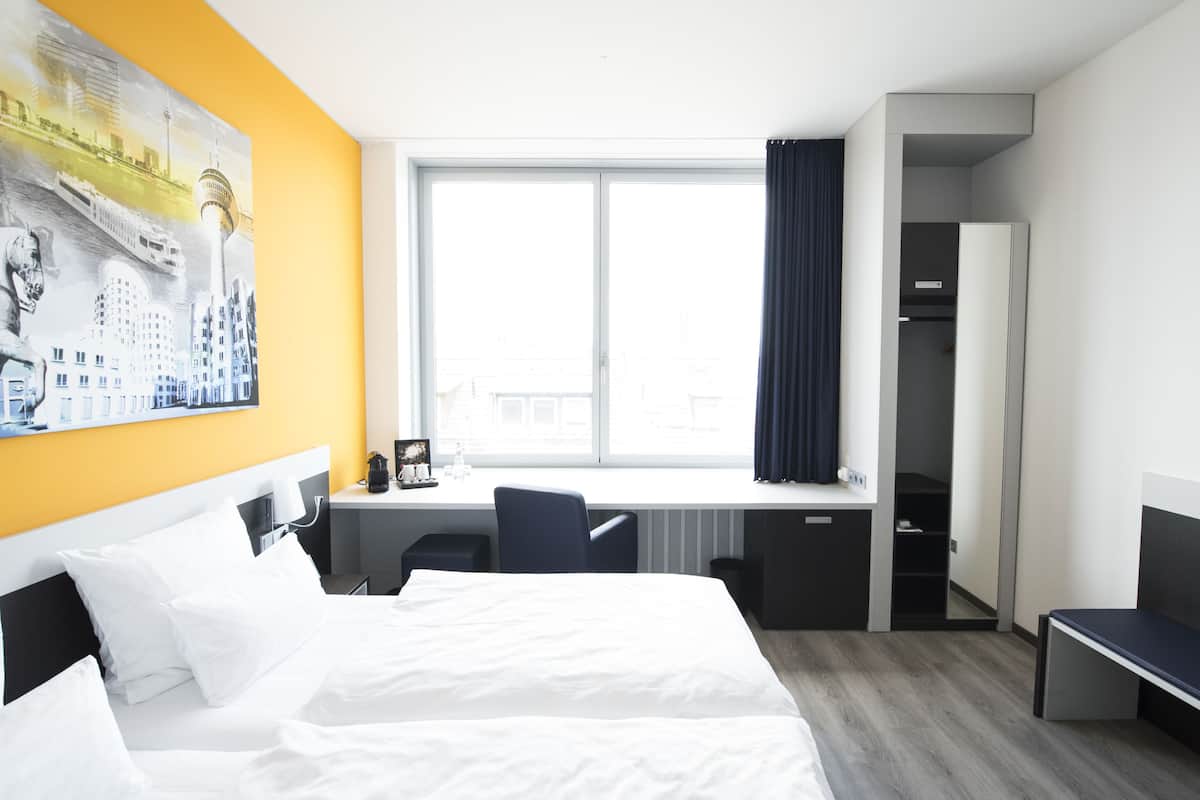 Habitació d'hotel amb llit, escriptori, cadira, armari i una finestra gran.